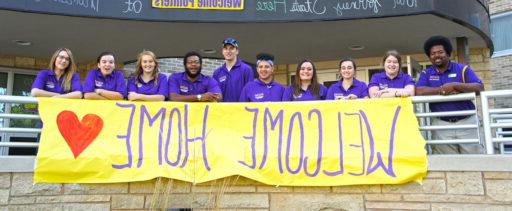 Residence life students and staff outside of hall with welcome home banner.